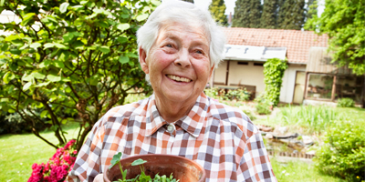 An older adult smiling and holding a flower pot in a beautiful yard