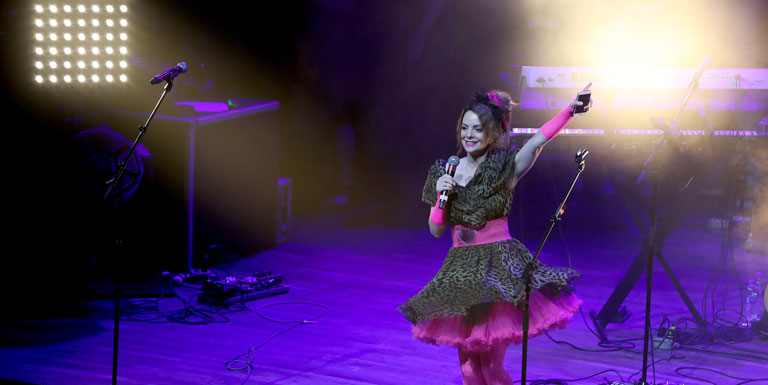 Kimberly Williams-Paisley stands onstage holding a microphone, dressed for a 1980s theme.