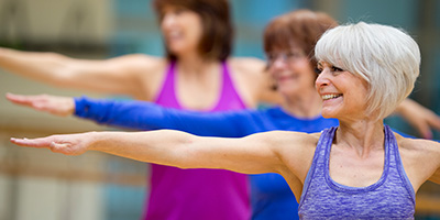 An older woman in purple does the warrior yoga pose.