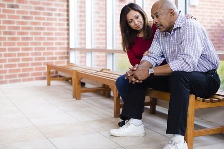 A woman comforts an older man seated next to her.