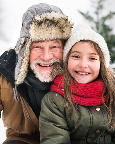 Grandfather and granddaughter wearing winter hats and smiling in the snow