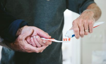 A close up of a man holding a toothbrush and another man putting toothpaste on the bristles.