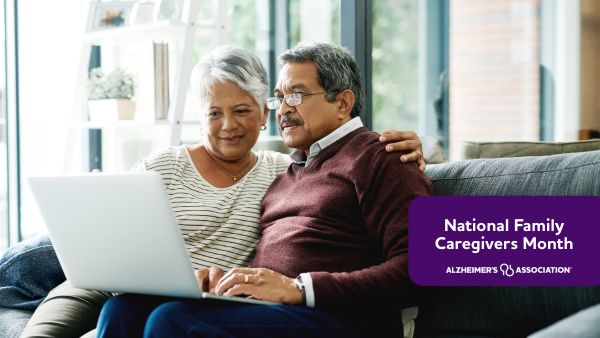 An older couple reads information on a laptop while sitting together on the couch