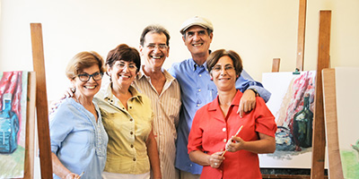 Group of older adults smiling together in front of painting canvases.