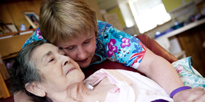 A woman wearing an Alzheimer's Awareness bracelet hugs an older woman